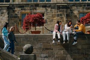 Two students walking down the steps and three students sitting on the wall chatting in the inner quad