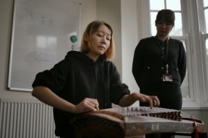 Student playing GuZheng under staff supervision
