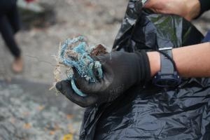 Image of a hand wearing a black rubber glove holding blue rope to put into a black bin bag