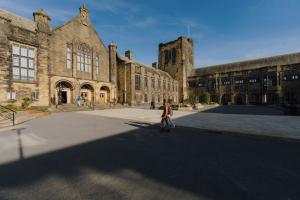 Prif Adeilad y Celfyddydau, sydd wedi'i oleuo'n hyfryd, y tu hwnt i'r Cwad Allanol, wrth i ddau fyfyriwr gerdded tuag at ei fynedfa o gyfeiriad y llyfrgell.