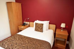 Single bed with white linen and brown accents, two night stands, wardrobe and feature wall in red