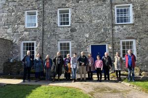 A group of twelve people standing in front of a stone house