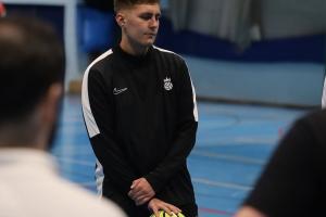 Glenn Swain standing on indoor football pitch in black kit with a yellow football