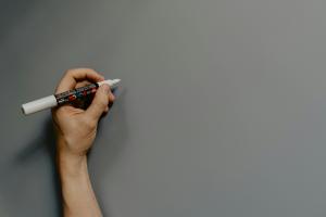 Hand holding a white Posca marker over a grey background