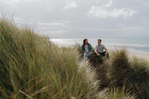 Dau fyfyriwr yn eistedd yn sgwrsio yn y twyni