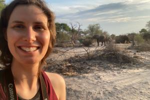 Penny Downes standing in the savannah with three elephants in the background