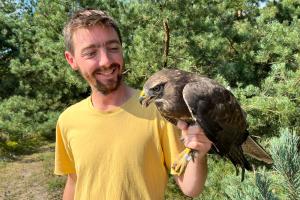 Will holding an eagle with vegetation in the background