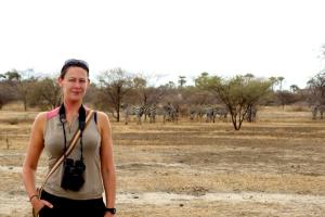 Caroline standing in the African savannah with a herd of zebra in the background