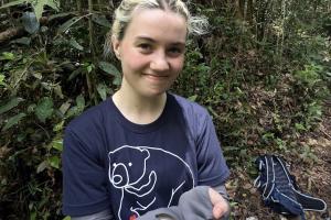 Amelia Harvey is standing in a forest with a small snake in her hands