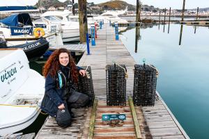 Project manager posing with oyster nurseries above the pontoon at the marina