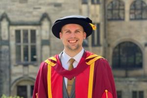 Llun o Matthew yn ei wisg graddio goch.