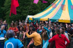 People in a field in a festival with a green and yellow marquee in the background