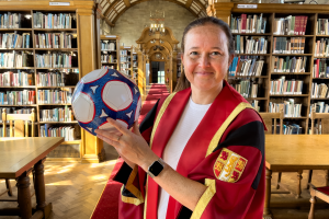 Image of Cheryl Foster wearing a red and gold graduation robe, holding up a football