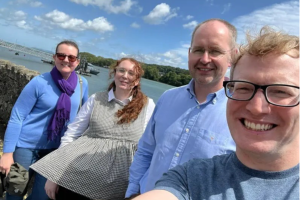 Four people taking a selfie in front of the Menai Straits, all smiling