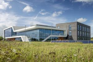 A modern building with large glass sections stands behind a grassy area with solar panels.