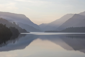 Ffotograff o Eryri wrth fachlud haul, gyda llyn yn y blaendir a mynyddoedd yn y cefndir