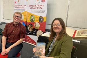 Dr Shaun Evans sits on the left, in front of the ISWE banners. Dr Lowri Ann Rees sits on the right, holding a copy of Shaun's book.