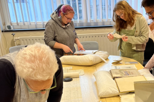 A group of four students gathered around a table looking at books laid out on white cushions in the archives