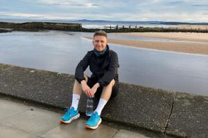 Joseph in running gear sitting in front of the sea with a bottle of water