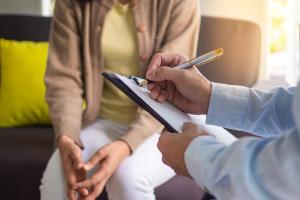 A person is writing notes on a clipboards and another person is sitting opposite 