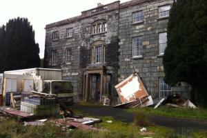A photograph of a Georgian mansion in a dilapidated condition, with a white lorry, building materials and debris in the foreground. 