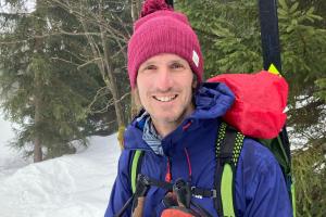 Dr Sam Oliver with snow backdrop wearing a bobble hat and outdoor warm clothes smiling at the camera.
