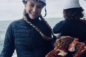 PGR researcher Lexi Reynolds is on deck of a research vessel at sea holding a large crab 
