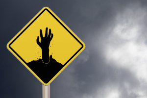 Yellow road sign with a black image of a zombie hand coming out of it.