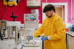 Picture of a student in a lab wearing yellow coat, blue glows and protective eyewear