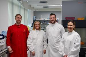 A group of people smiling at the camera wearing lab coats