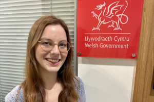 Laura Czerwinska smiling to camera with the Welsh Government logo behind on the wall