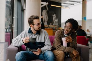 Two students socialising in a café, one is holding a hot drink and another is holding a smoothie.