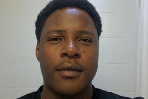 an image of a student (mark) looking into the camera taking a photo. the student is wearing a black shirt and has a small smile. the student is standing in a blank white background