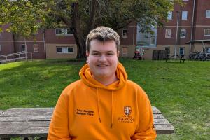 an image of aiden from campus life wearing an orange campus life hoodie. He is sitting on a bench outsidean image of aiden from campus life wearing an orange campus life hoodie. He is sitting on a bench outside
