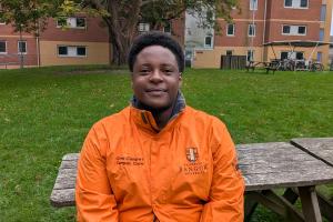 An image of Mark from campus life wearing an orange campus life coat. He is sitting on a bench outside 