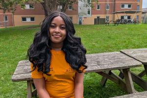 An image of Nokutenda from campus life wearing an orange campus life tshirt. She is sitting on a bench outside 