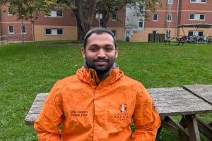 An image of Steffan from campus life wearing an orange campus life coat. He is sitting on a bench outside 