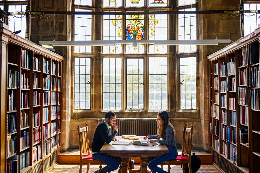 Students working at the Main Arts' Shankland Library with stained glass window in the background