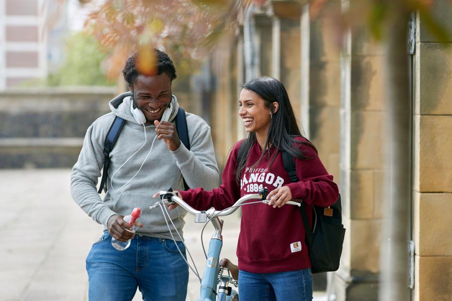 Two students walking and pushing a bike outside the Main Arts building