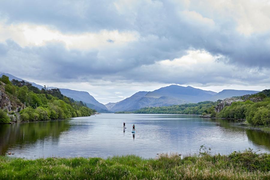 Dau fyfyriwr ar fyrddau padlo ar Lyn Padarn