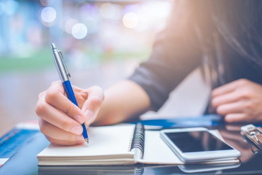 Student at desk with phone and writing.