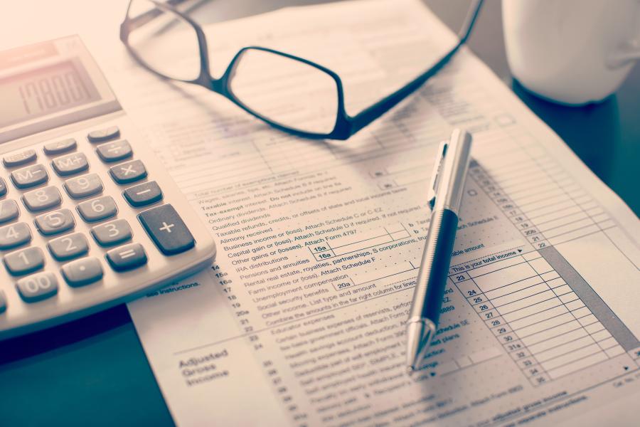 Shows a working desk including accountancy sheet, glasses, calculator and pen.