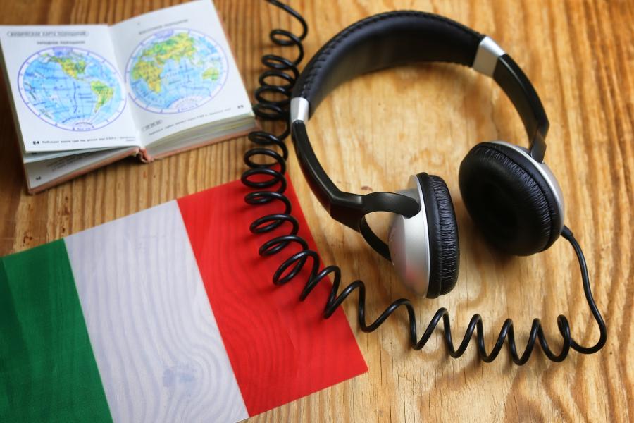 Headphone and book on a desk with an Italian flag.