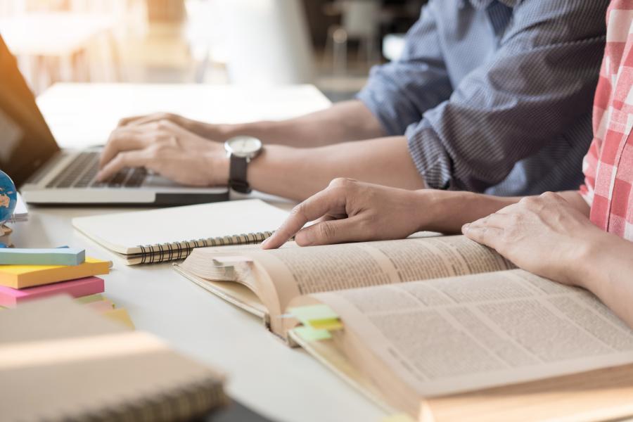 Two students studying together with books and a laptop 