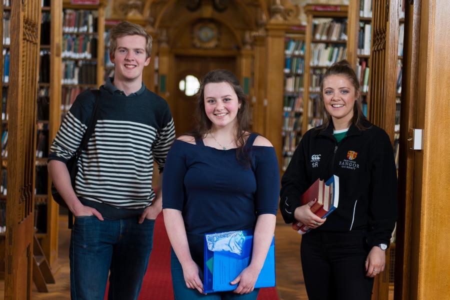Three students with books standing in the Shankland library