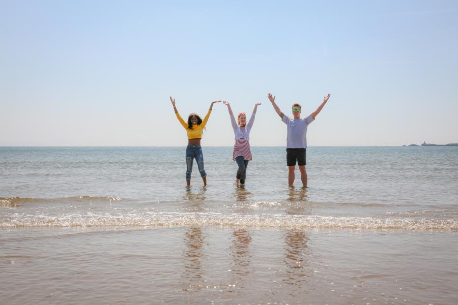 Three students dancing in the ocean at the beach