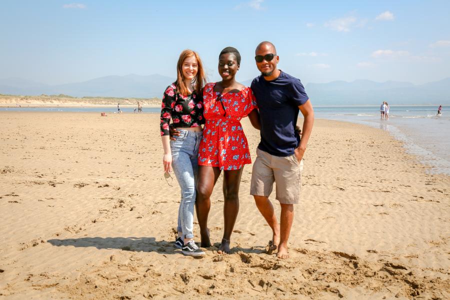 Three students stood on the beach enjoying the sun