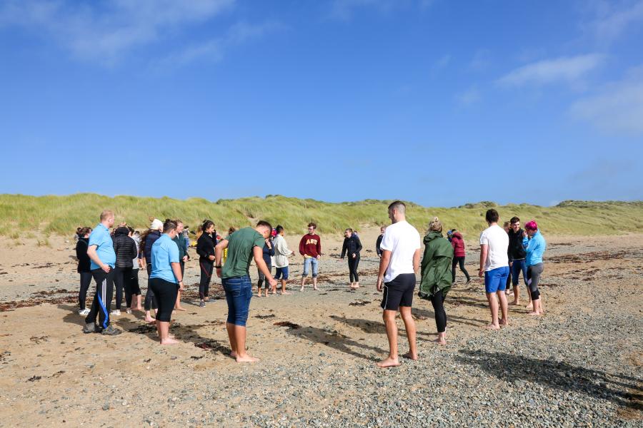 Grŵp o fyfyrwyr yn cymdeithasu a chwarae gemau ar y traeth yn yr haul