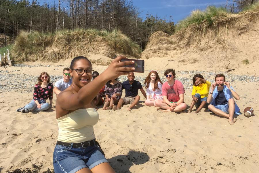 Grŵp o fyfyrwyr yn mwynhau'r haul a thynnu hunlun ar y traeth