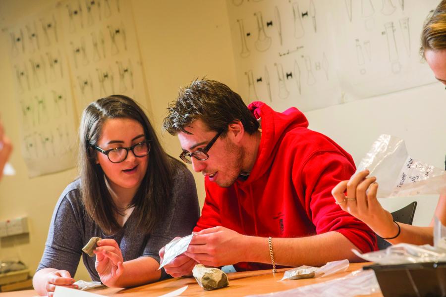 dau fyfyriwr archaeoleg yn astudio arteffactau mewn seminar archaeoleg